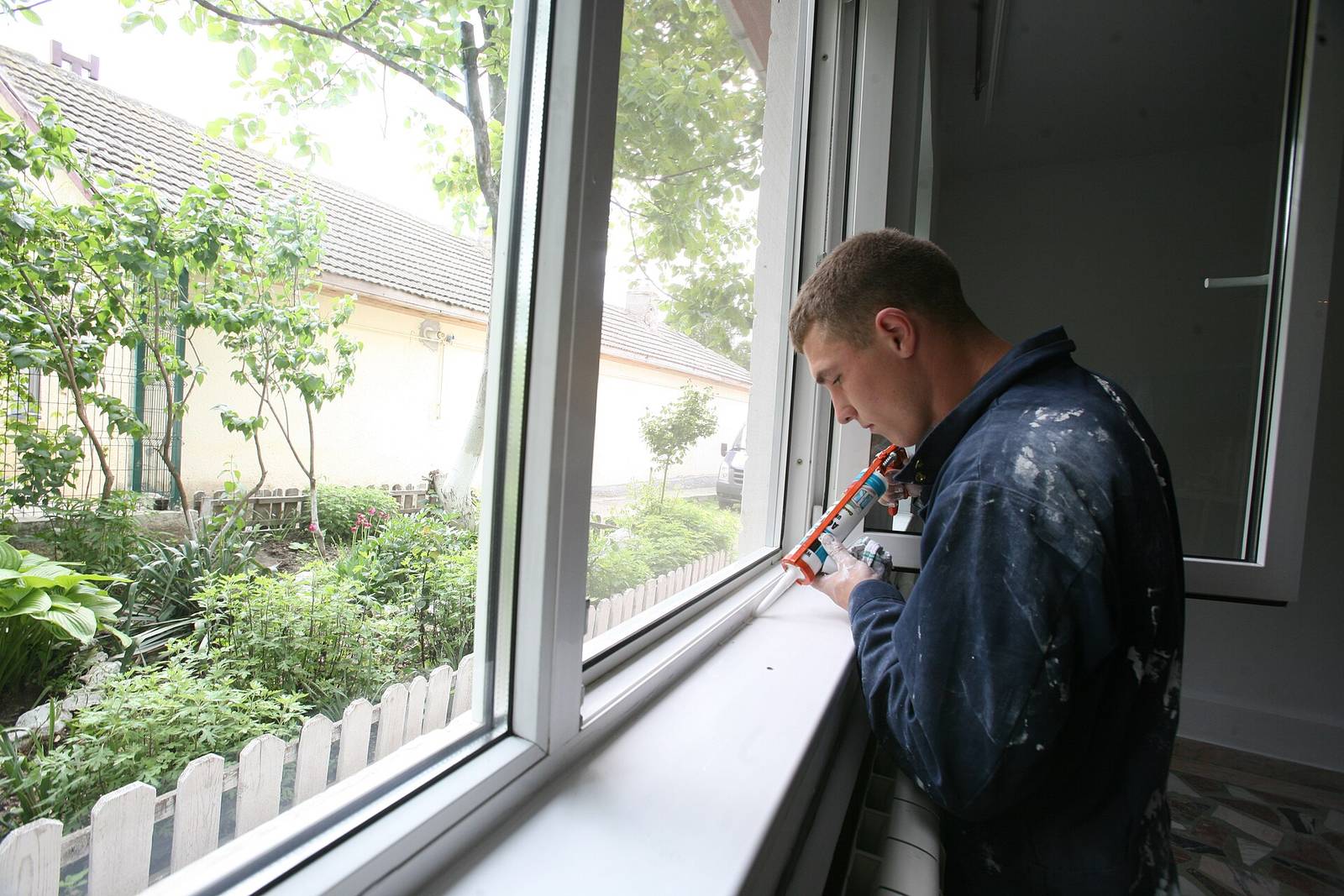 Vakman spuit met een kitpistool een voeg dicht langs de onderkant van een nieuw wit raam