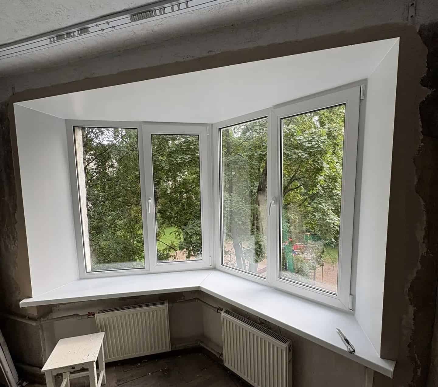 Nieuw geplaatst wit hoekraam met brede vensterbank in een kamer waar de muren nog niet afgewerkt zijn